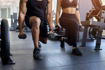 2 Menschen die einen Ausfallschritt im Fitnesstudio trainieren